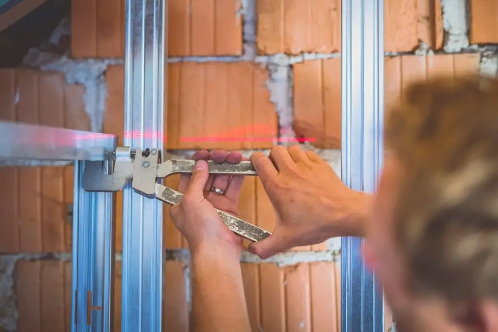 man using drywall studs to show when to glue drywall to studs 